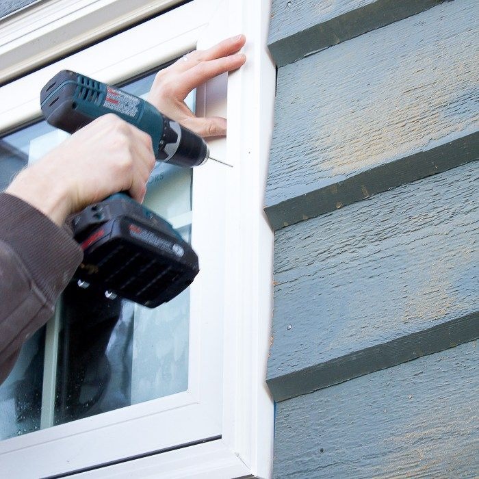 Professional installing exterior window frame with cordless power drill